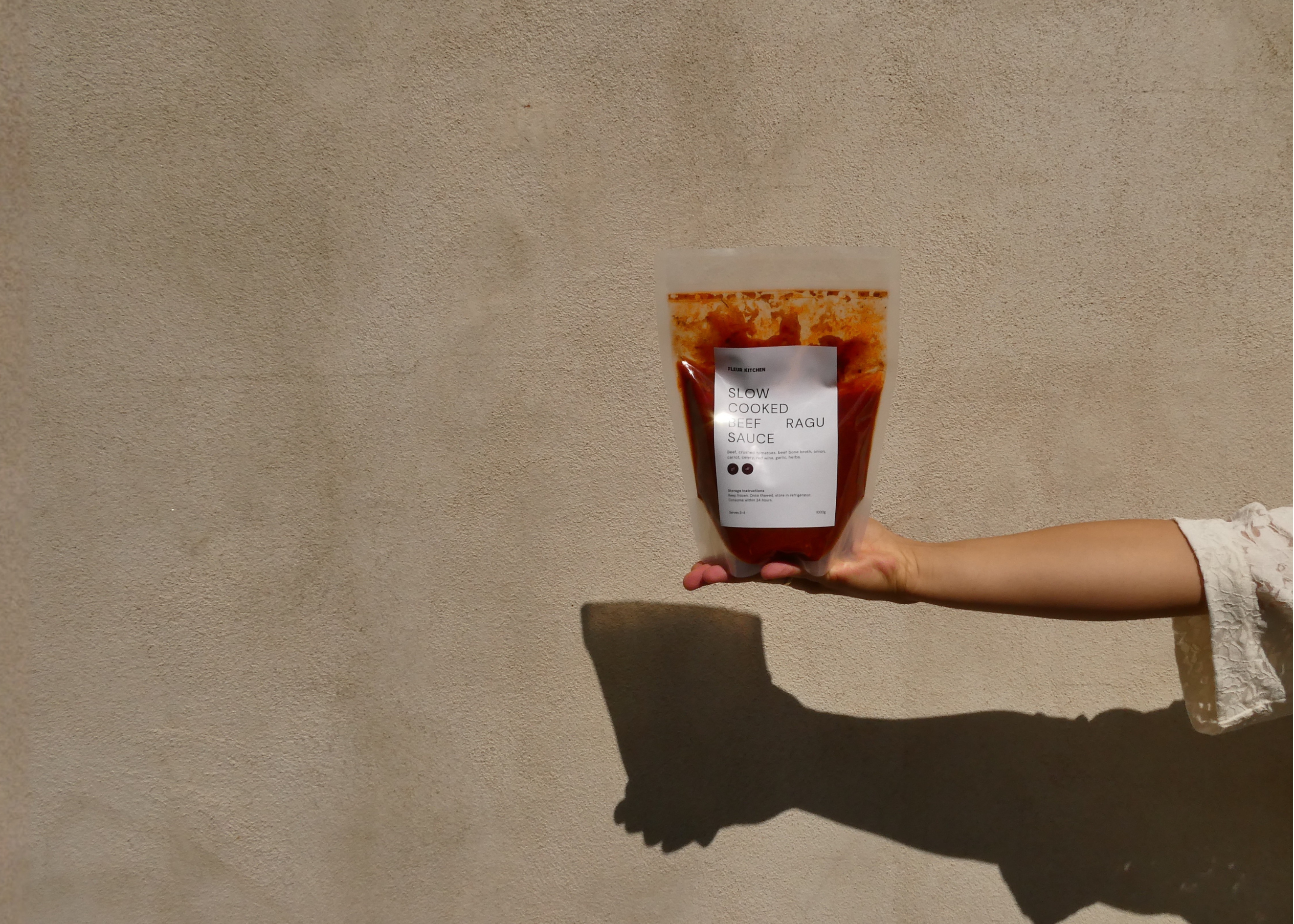 Hand holding a Fleur Kitchen ready-made meal against a wall